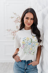 Woman wearing a white t-shirt with floral design and text, standing against a light background.