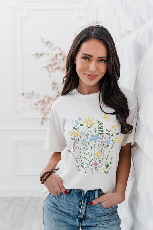 Woman wearing a white t-shirt with floral design and text, standing against a light background.