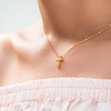 Gold necklace with a cross pendant on a person wearing a white top.