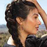 Woman with braided hair and gold hoop earrings against a blurred natural background