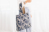 Person holding a blue tote bag with a white paisley pattern on a plain background
