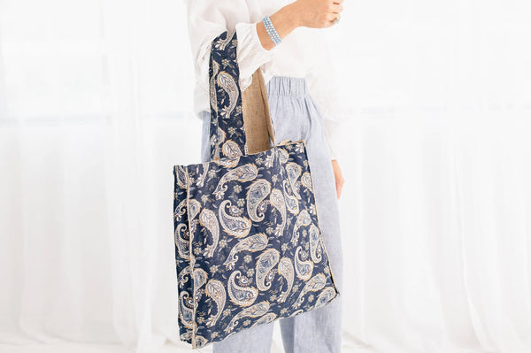 Person holding a blue tote bag with a white paisley pattern on a plain background